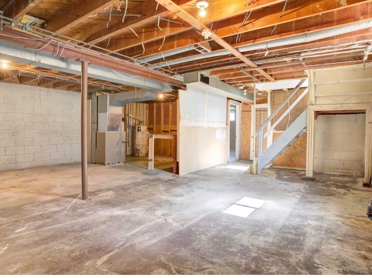 An unfinished basement with exposed joists and bare concrete floor